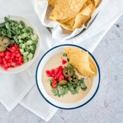 Creamy queso dip with diced tomatoes, green onions, chiles, and tortilla chips served in a bowl.