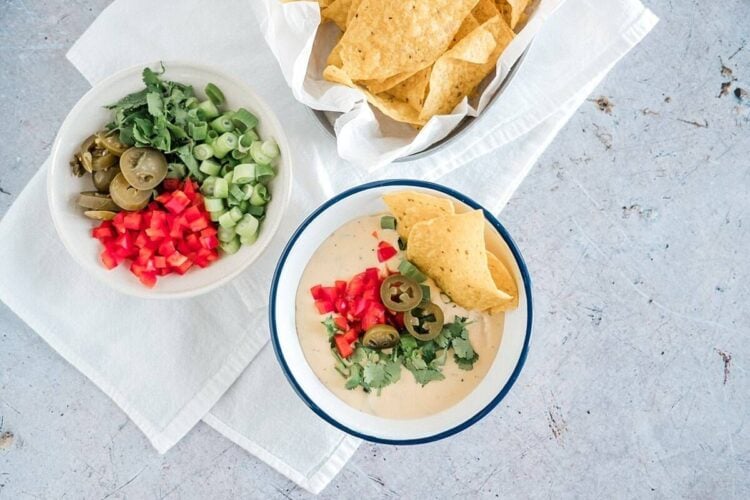 Creamy queso dip with diced tomatoes, green onions, chiles, and tortilla chips served in a bowl.