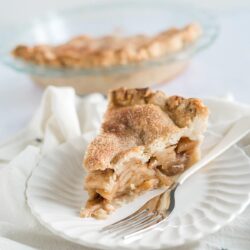 Buttered apple pie slice on a white plate with a fork, featuring flaky crust and warm apple filling.