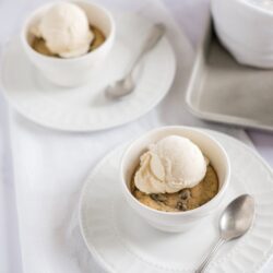Creamy vanilla ice cream served in a small white bowl with chocolate chip cookies on a white plate.