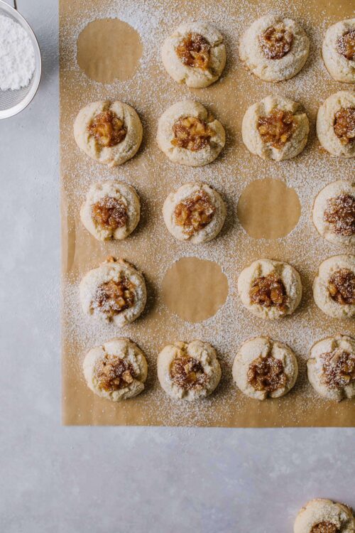 Freshly baked thumbprint cookies with caramel filling on parchment paper, dusted with powdered sugar.