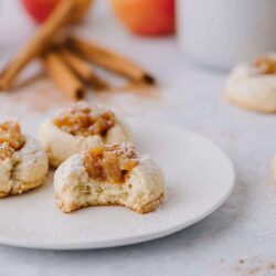 Buttery caramel thumbprint cookies with apple filling on a white plate, sprinkled with powdered sugar. Perfect holiday dessert.