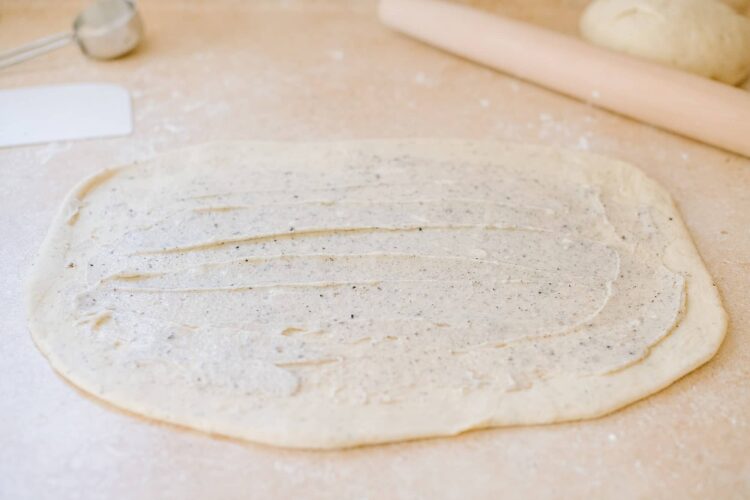 Thinly rolled pizza dough with specks of herbs on a floured surface.