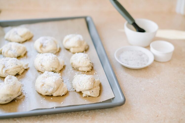 Cream cheese cookies on baking sheet with powdered sugar, baking supplies and utensils in background.