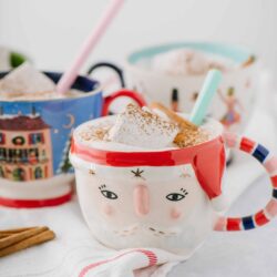 Colorful Christmas-themed mug with hot chocolate topped with marshmallows and cinnamon, festive holiday beverage.