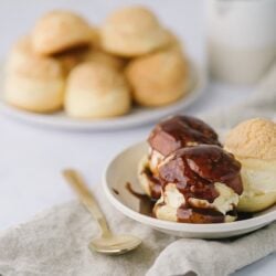 Freshly baked ice cream profiteroles with chocolate sauce and vanilla ice cream on a white plate.