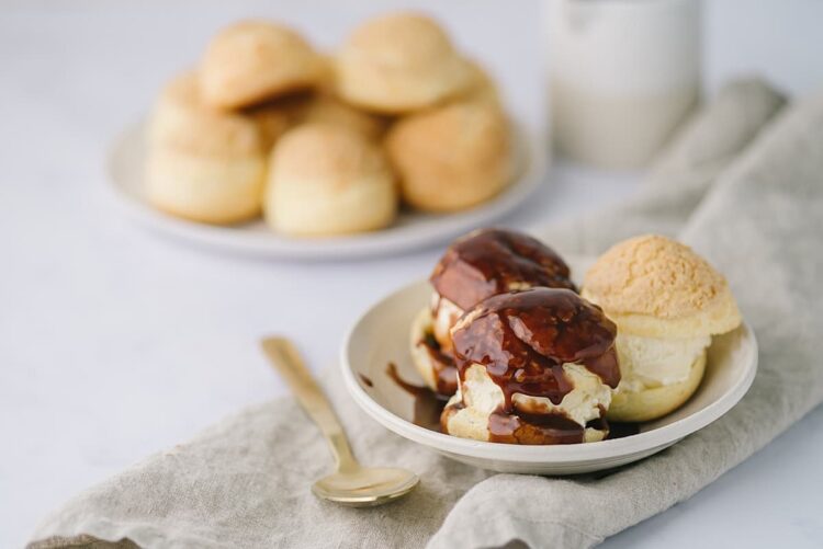 Freshly baked ice cream profiteroles with chocolate sauce and vanilla ice cream on a white plate.