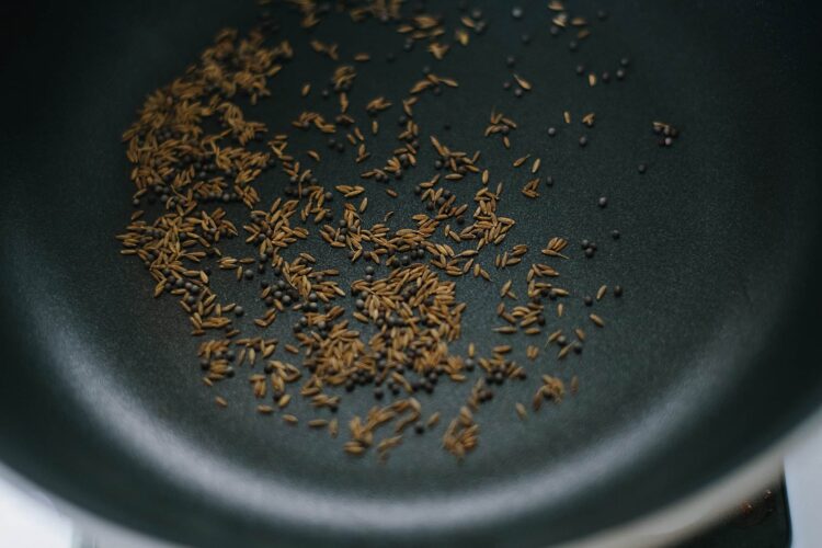 Roasted cumin seeds and coriander seeds in a black frying pan.