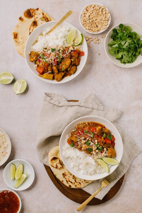 Savory chicken curry with rice and flatbread, topped with fresh herbs and lime wedges.