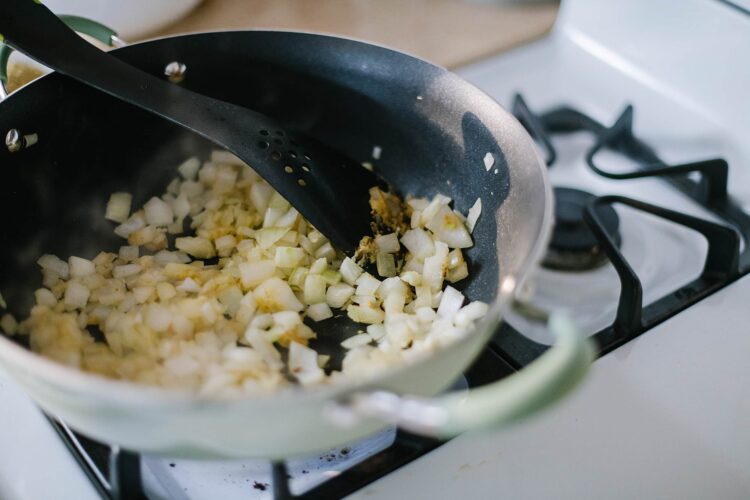 Diced onions cooking in a frying pan on a stovetop, preparing for baking or cooking.