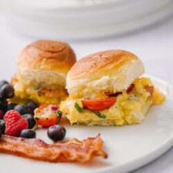 Fluffy breakfast biscuit sandwich with scrambled eggs, cherry tomatoes, bacon, and fresh berries.