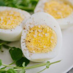 Soft boiled eggs with flaky salt on a white plate, garnished with fresh green watercress.