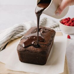 Rich chocolate pound cake being drizzled with glossy chocolate glaze.