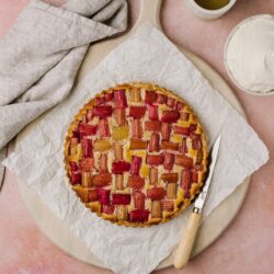 Rhubarb strawberry tart on parchment paper with cream and honey on a wooden board.