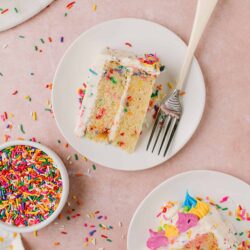 Colorful sprinkle cake slices with rainbow sprinkles on pink background.