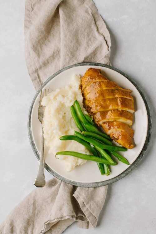 Juicy roasted chicken breast with gravy, creamy mashed potatoes, and green beans on a white plate.