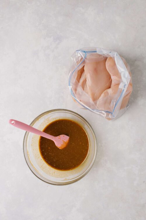 Boneless chicken breasts in plastic bag with marinade in glass bowl on white surface, sourced from Baked Bree, perfect for chicken recipes.