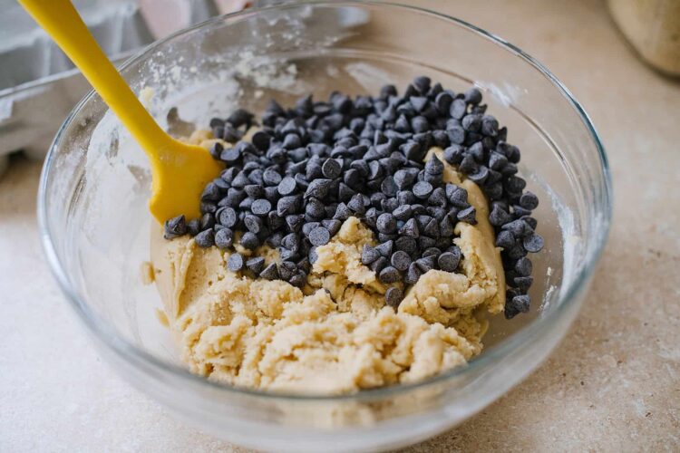 Creamy cookie dough with chocolate chips in a glass mixing bowl for baking recipes.