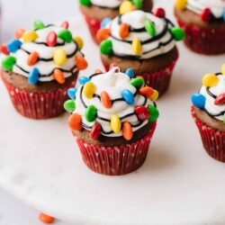 Colorful Christmas cupcake with candy decorations and white frosting on a white marble cake stand.