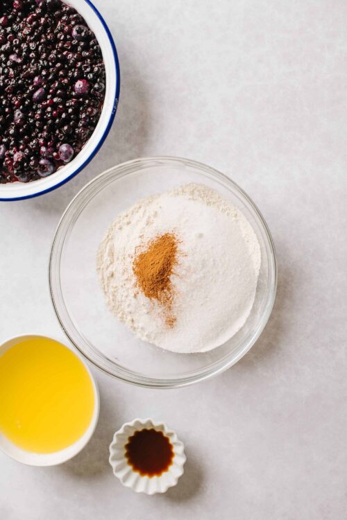 Fresh frozen blueberries, flour, cinnamon, butter, and vanilla extract for blueberry muffin baking.