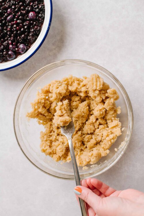 Buttery pie crust dough in a glass bowl with a metal fork.