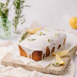 Lemon drizzle cake with white glaze and fresh daisies on a wooden board.