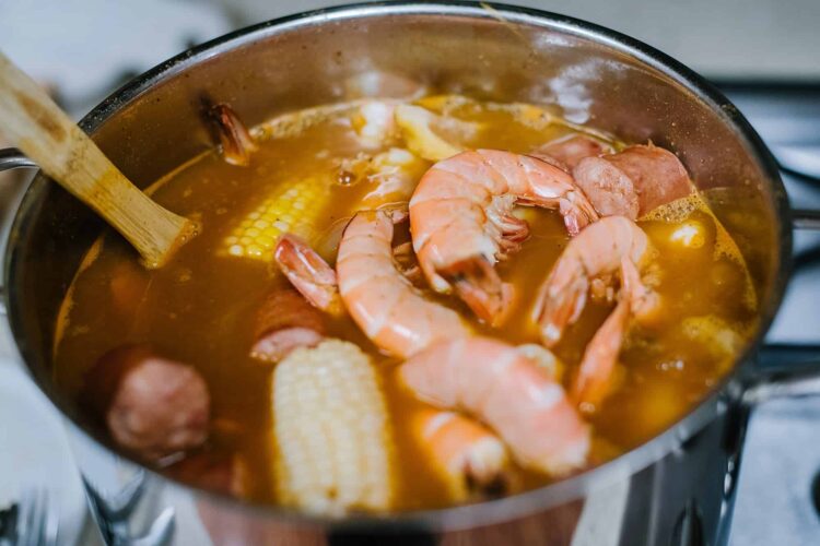 Boiling seafood stew with shrimp, corn, and sausage in a stainless steel pot.