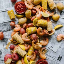 Fresh seafood and vegetable platter with shrimp, corn on the cob, new potatoes, lemon wedges, and cocktail sauce.