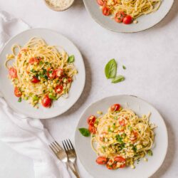 Delicious cherry tomato pasta with herbs and cheese on white plates, ready to serve.