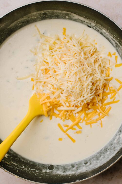 Creamy cheese sauce with shredded cheddar and Monterey Jack cheese melting in a skillet.
