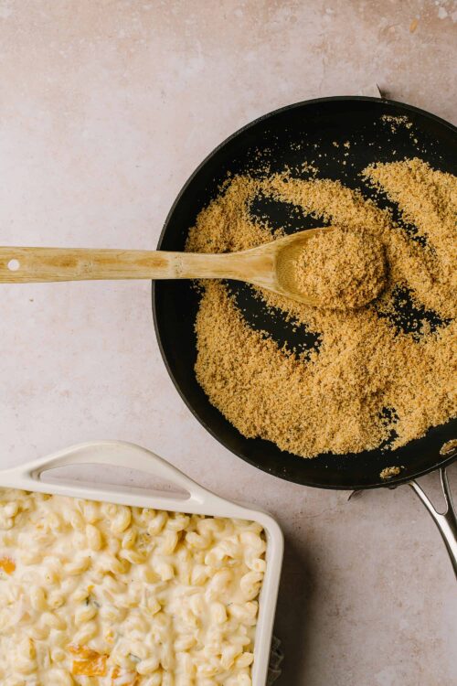 Golden breadcrumbs in a black skillet with a wooden spoon for homemade crispy topping.