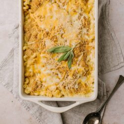 Creamy baked mac and cheese in a white casserole dish with sage garnish.