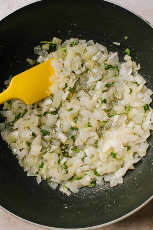 Sautéing chopped onions and green herbs in a skillet for delicious recipes.