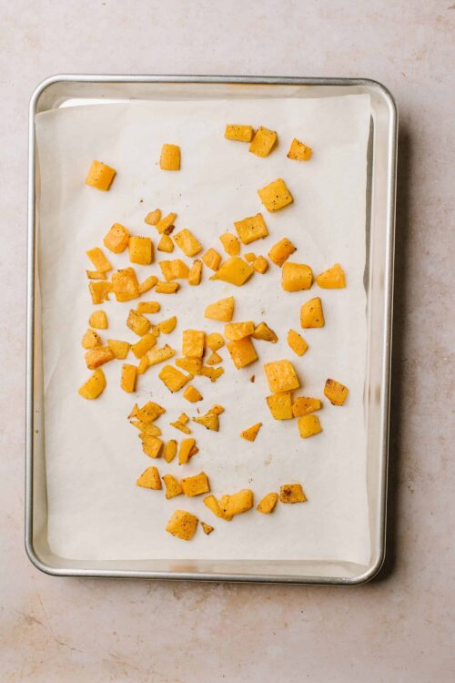 Crispy roasted sweet potato cubes on baking sheet with parchment paper.