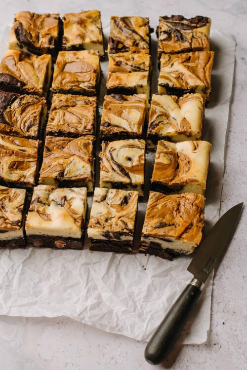 Marbled cheesecake brownies with peanut butter swirl on parchment paper.