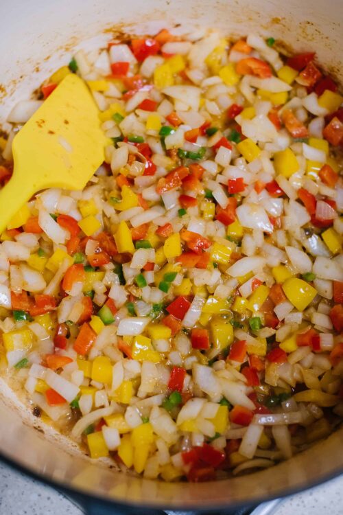 Diced onions, red, yellow, and green bell peppers cooking in a skillet, ready for a savory recipe.