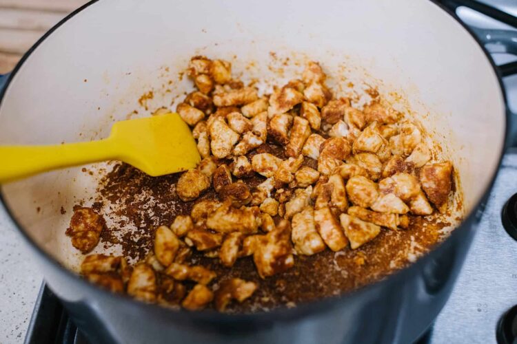 Chicken cooking in a pressure cooker with a yellow spatula inside.