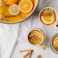 Lemon and orange infused hot beverage with cinnamon and cloves in mugs; cozy winter drink.