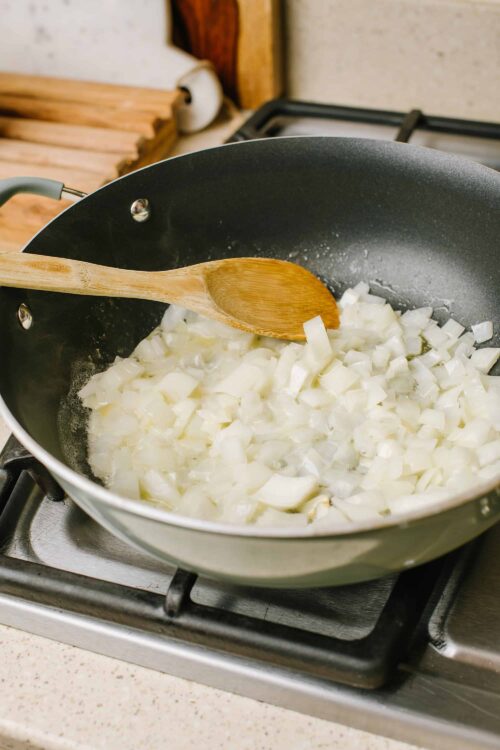 Sautéing chopped onions in a non-stick skillet over a gas stove for cooking.
