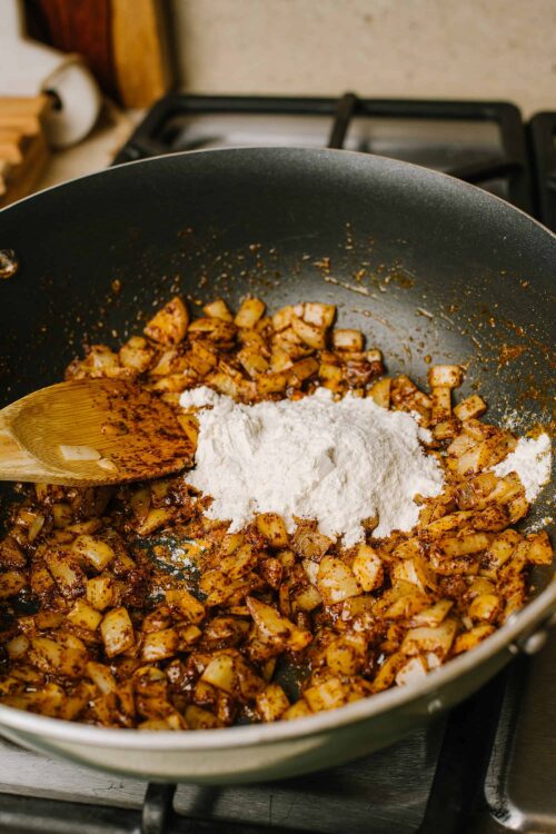 Sautéed onions with spices and flour in a black skillet for flavorful cooking.