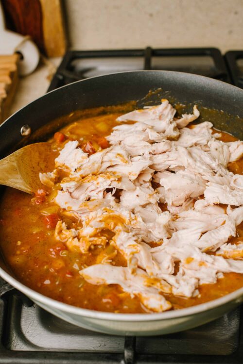 Shredded cooked chicken added to a flavorful broth in a skillet.