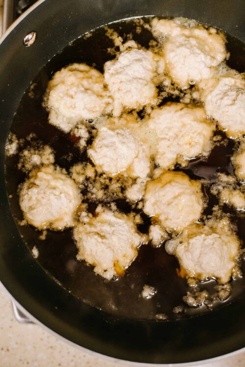 Fried chicken meatballs cooking in a skillet with hot oil, crispy and golden exterior.