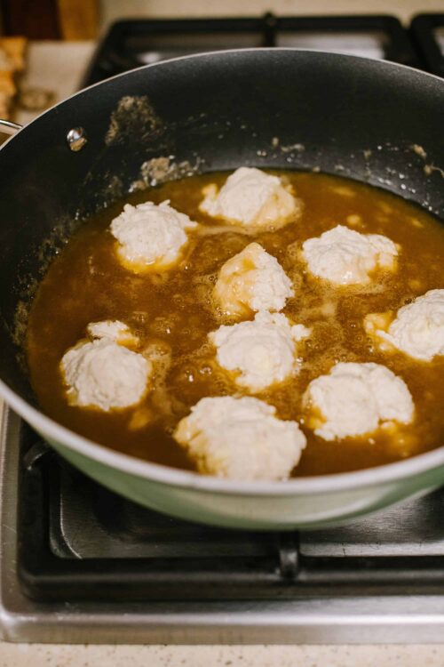 Soft Oreo cookie dough balls frying in caramel sauce in a green skillet.