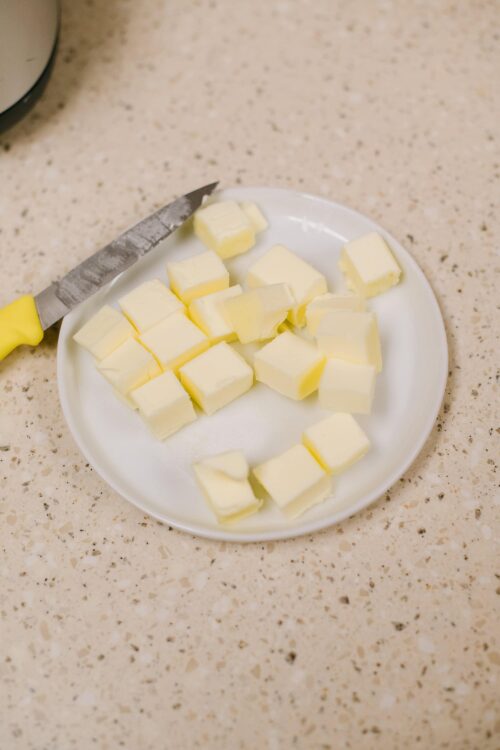 Creamy white chocolate chunks on a plate with a yellow-handled knife on a speckled countertop.