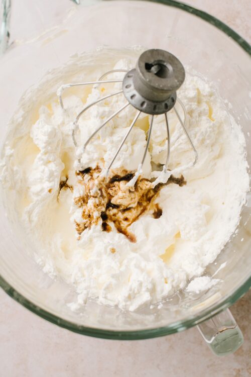 Cream cheese and sugar mixing in a glass bowl with a hand mixer attachment for baking.