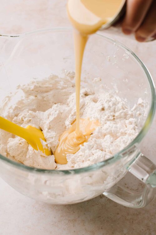 Fluffy flour mixture with creamy liquid being poured in, for baking recipes.