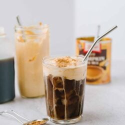 Frosted iced coffee with whipped cream and cinnamon on top, served in a glass with a straw.
