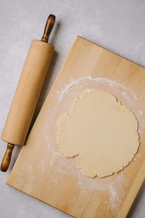 Rolled out cookie dough on wooden baking board with rolling pin for baking recipes.