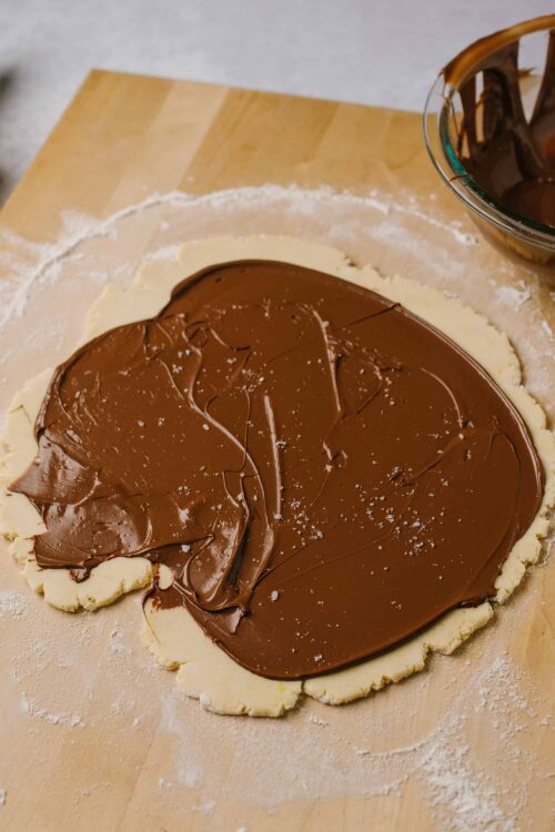 Rich chocolate spread on rolled out pie crust ready for baking.