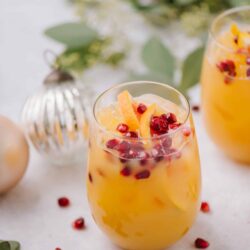 Refreshing peach and pomegranate fruit cocktail with citrus slices in clear glass glasses.